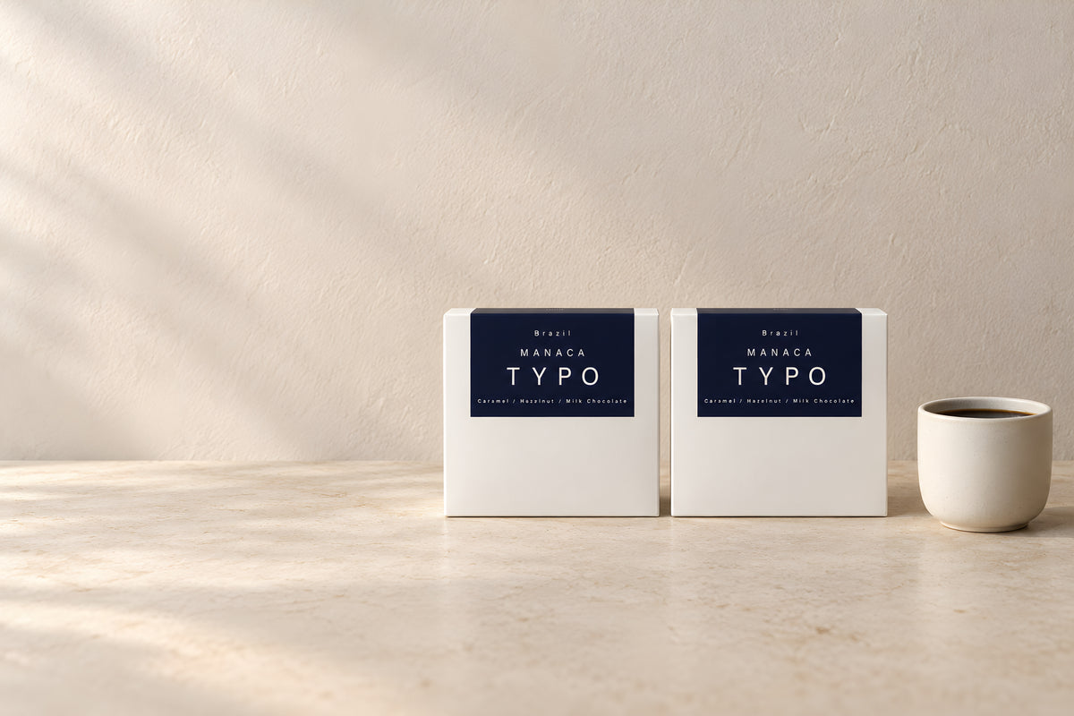 Two Typo Manaca coffee cartons beside a cup of coffee